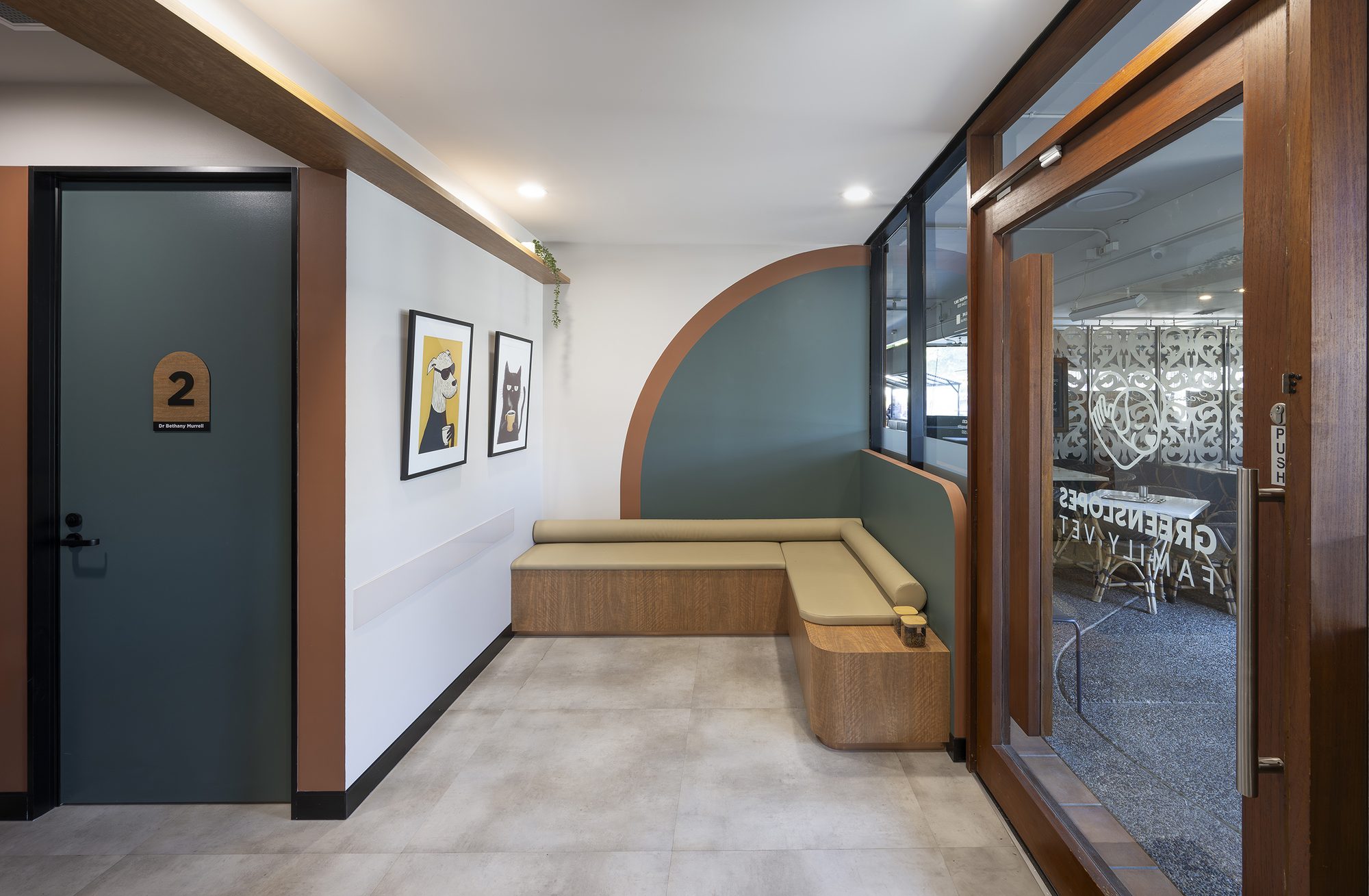 Clinic corridor with a curved timber archway, a numbered consulting room door and a built-in bench seat