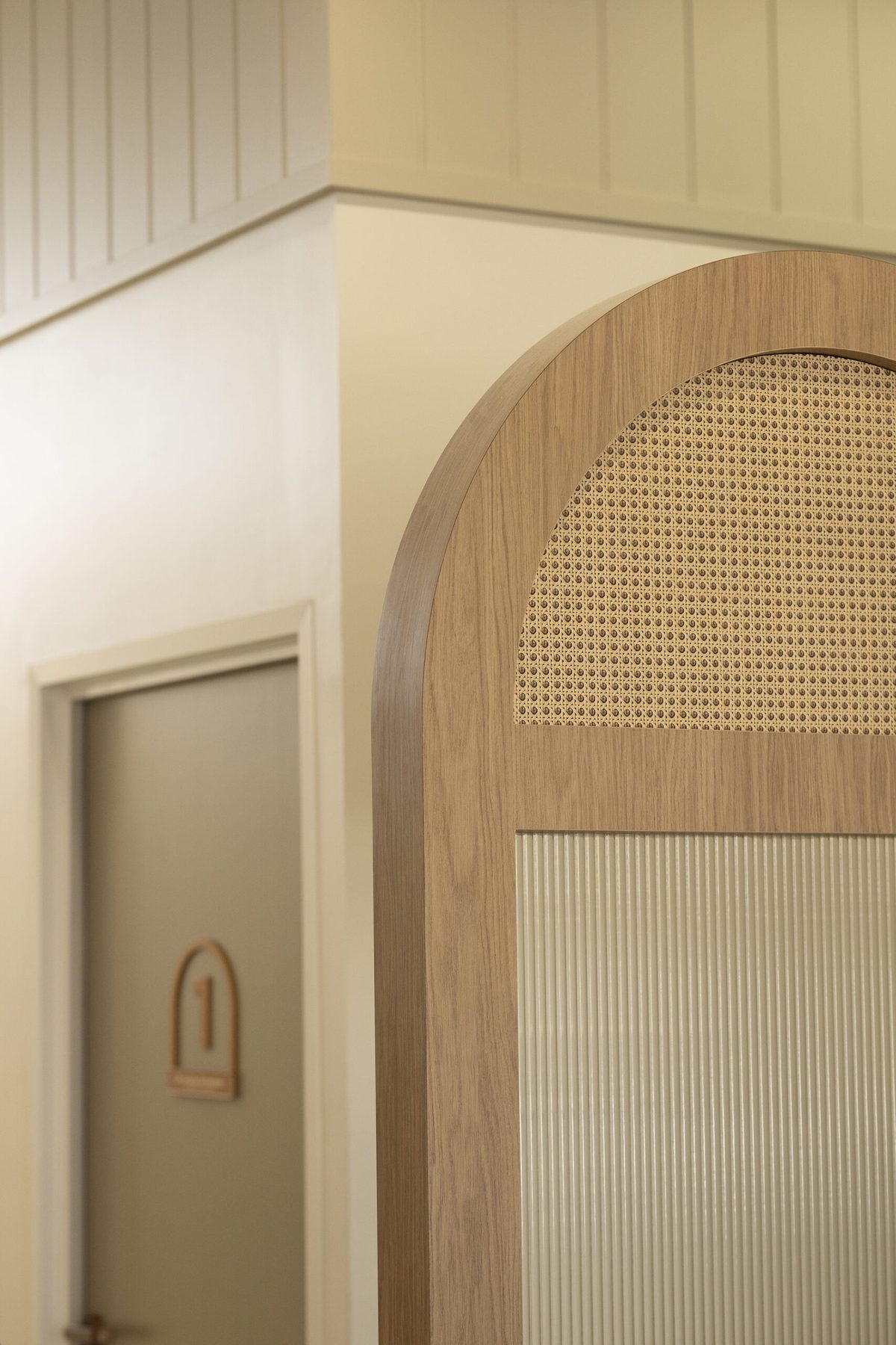 Curved oak archway with a cane panel in its head and a reeded glass panel below, beside a sage green door carrying an arched number one sign