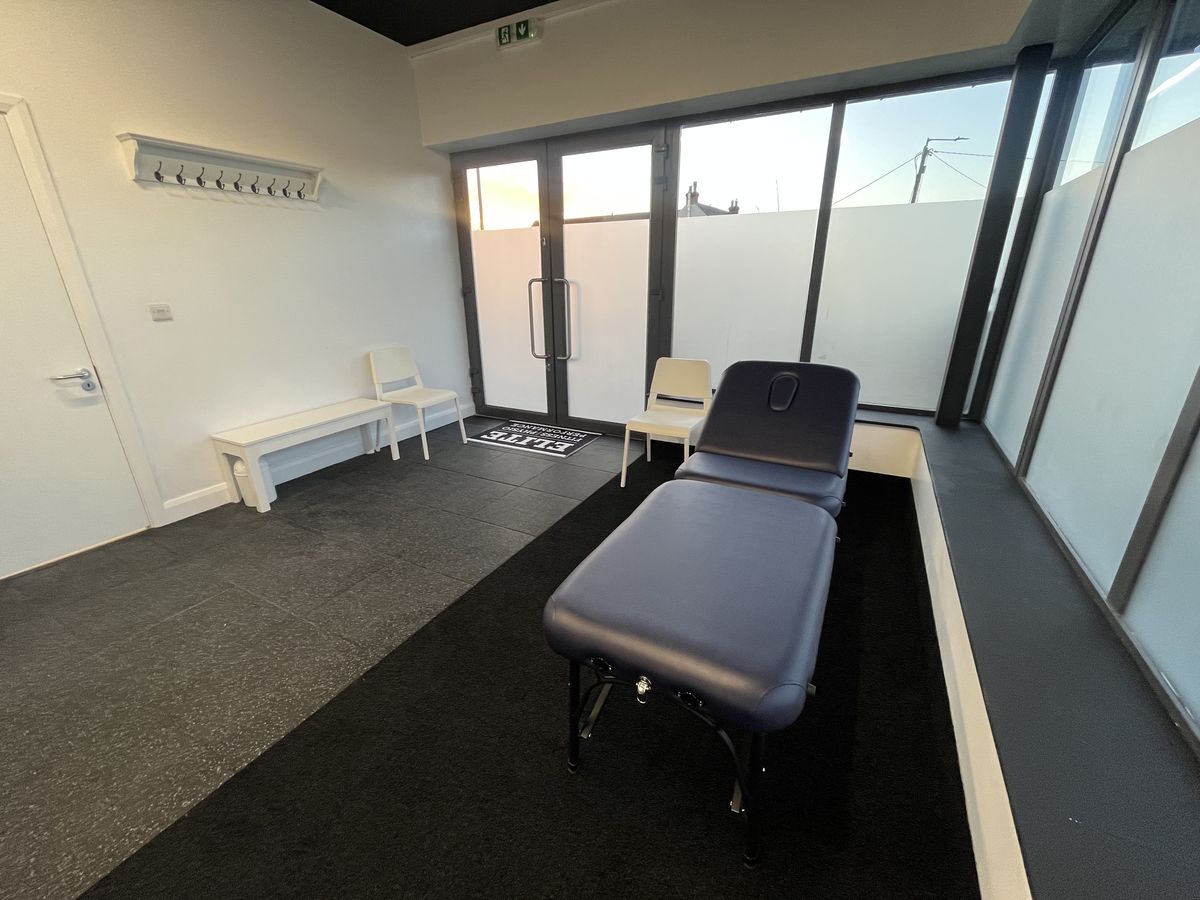 The physio treatment room with a table and bench beside a glazed door to outside