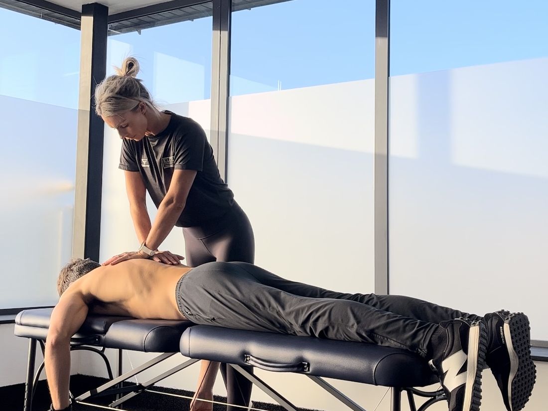 Laura treating a client lying face down on a treatment table beside a full height window