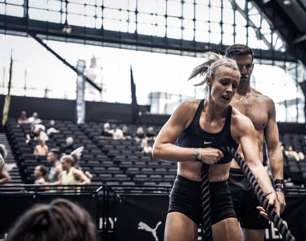 A competitor hauling a rope on a Hyrox competition floor with tiered seating behind