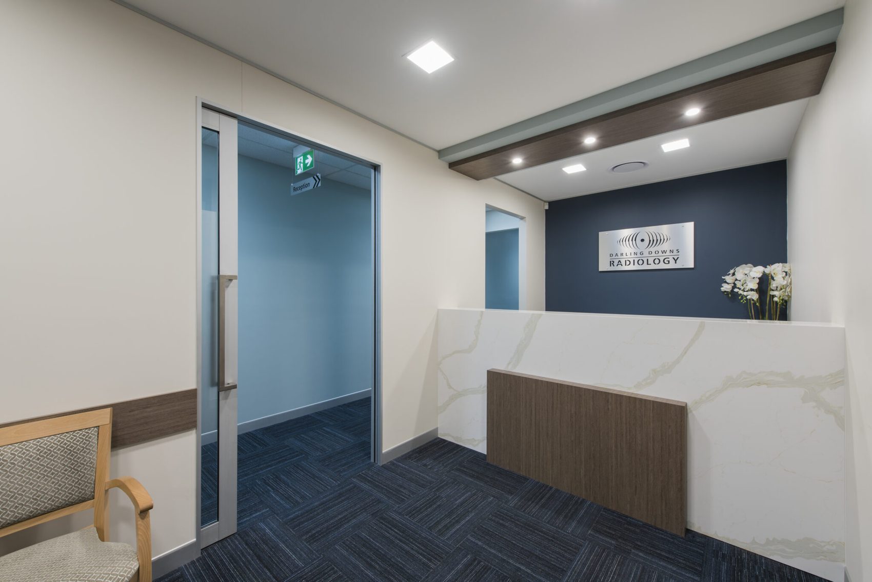 Stone reception counter in front of a navy feature wall carrying signage, beside a carpeted waiting area